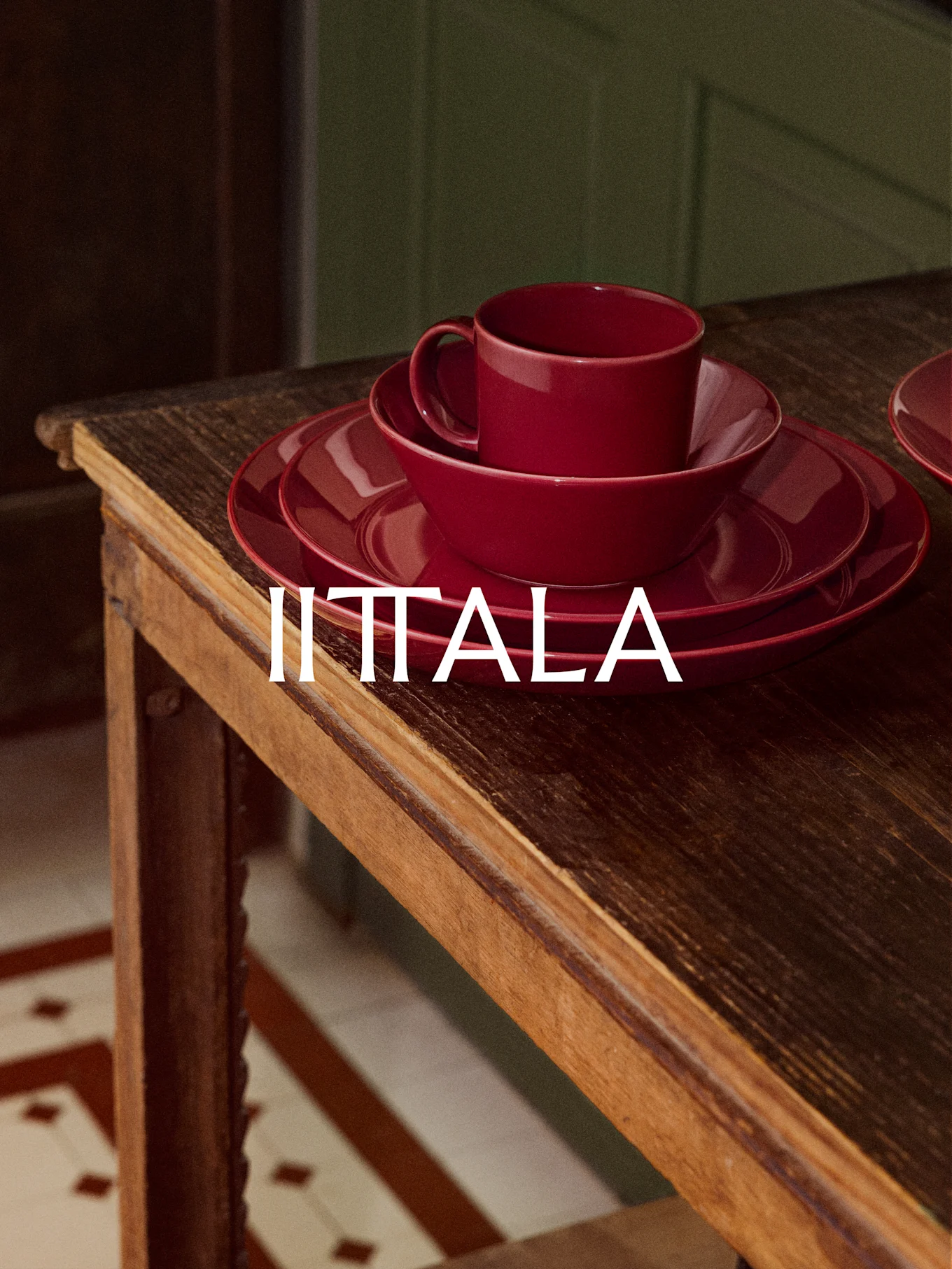 En stapel rött IITTALA-porslin, inklusive en kopp, skål och tallrikar, står på ett rustikt träbord.