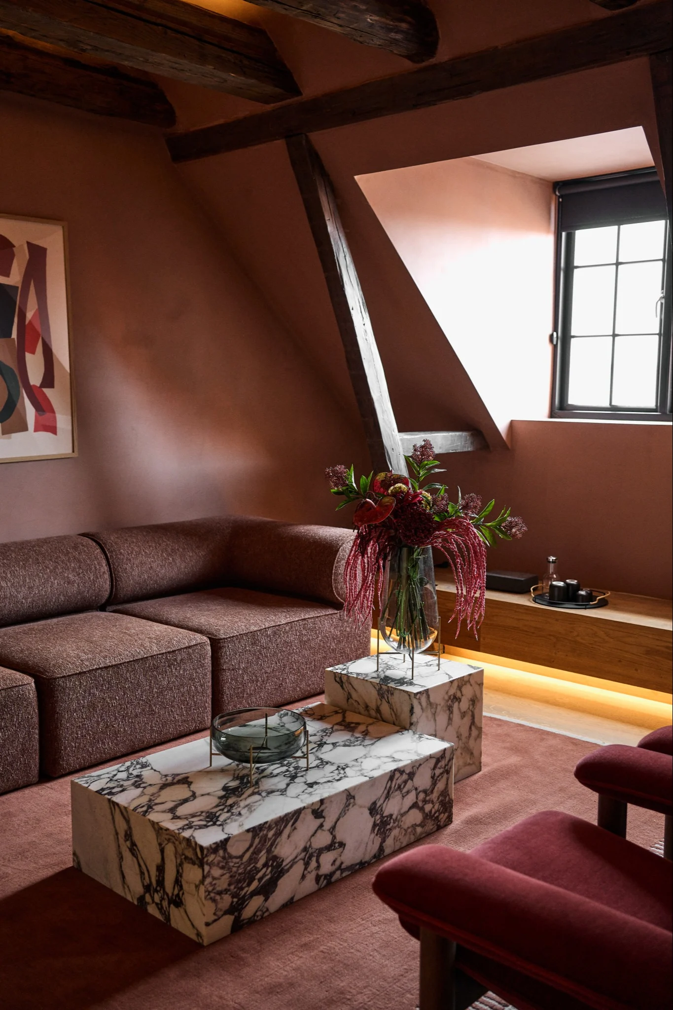 Ett vardagsrum med en vinröd modulsoffa och ett milerat stensoffbord som harmonierar med den vinröda inredningen.