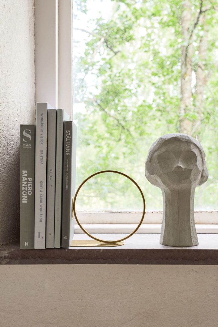 Stilleben i fönster med böcker, bokstöd i mässing och skulptur i form av ett kvinnoansikte från Cooee Design. 