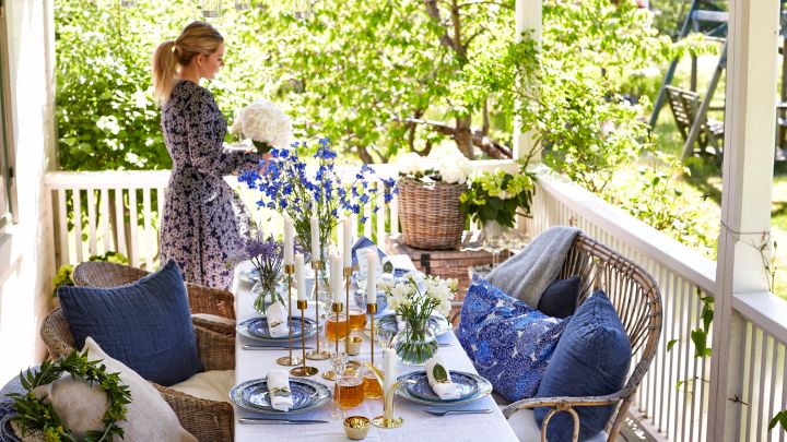 En blåvit och klassisk midsommardukning står på verandan med blåvitt porslin, ljusstakar i mässing och mycket blommor. 