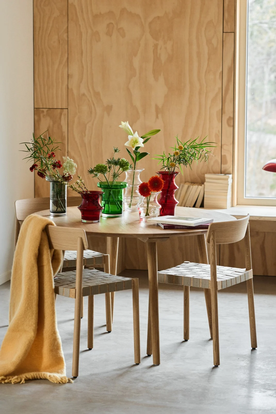 Ett matbord i ek med stolar i ek runt bordet och färgglada glasvaser på bordet från Kosta Boda i form av Pagod och Limelight-vaser i grönt, klarglas och rött. 