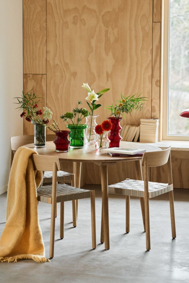 Ett matbord i ek med stolar i ek runt bordet och färgglada glasvaser på bordet från Kosta Boda i form av Pagod och Limelight-vaser i grönt, klarglas och rött. 