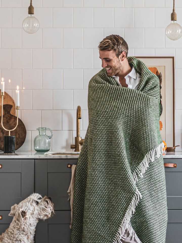 Influencern Hannes Mauritzson insvept i grön ullpläd hemma hos sig i samarbete med Nordic Nest. 