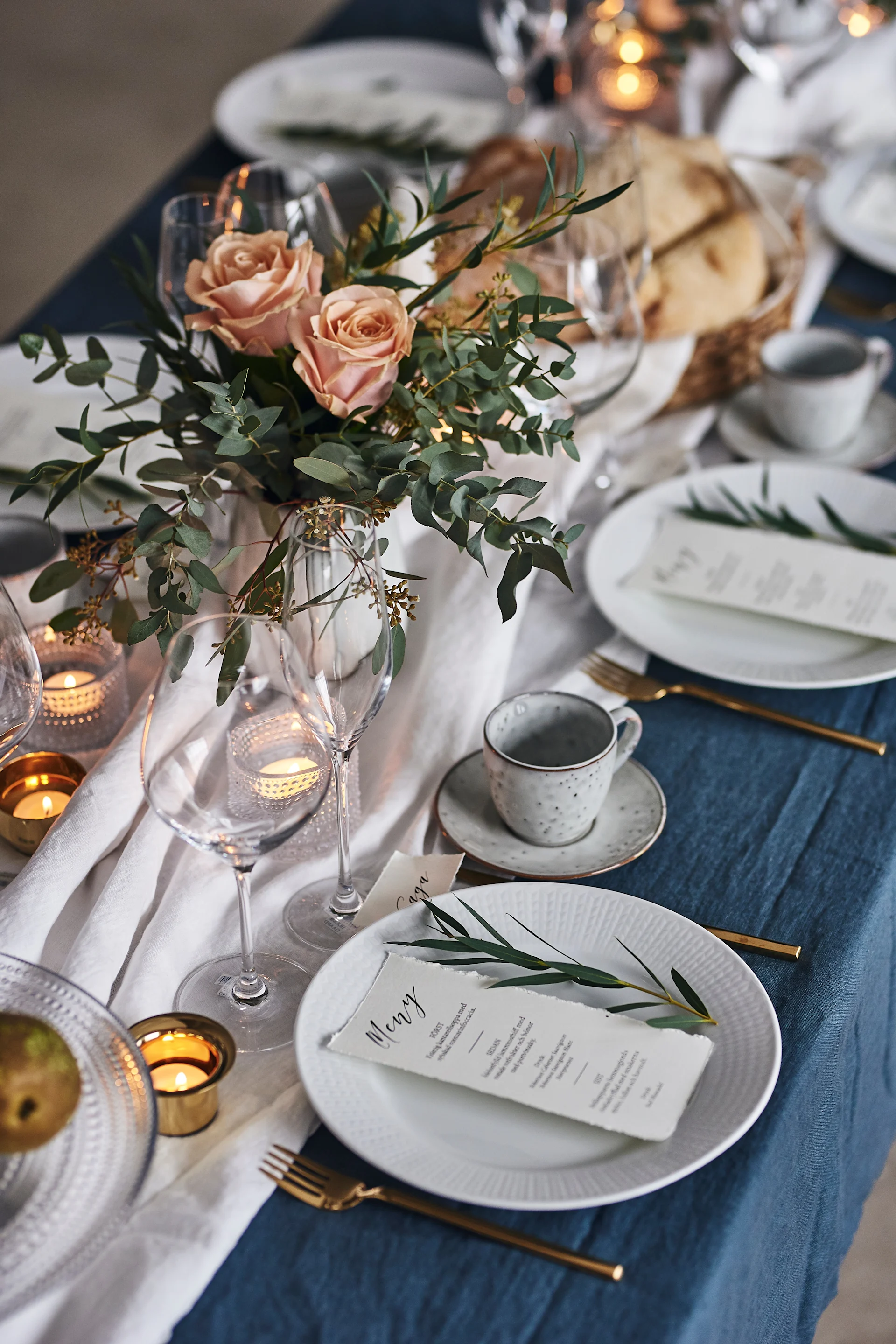 En löpare av vit linneduk och ljuslyktor från Skultuna i mässing och Kastehelmi ljuslyktor i glas  går längs med bordet.