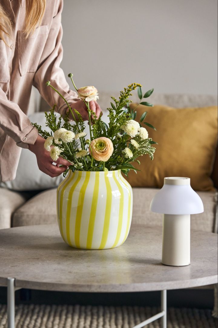 En blomsterbukett i färgglada Juice Wide vas i gult och vitt bredvid PC portable bordslampa i vitt från HAY.