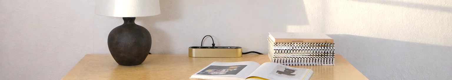 Guldfärgad grenkontakt med tre svarta uttag och en strömbrytare på en ljus yta.