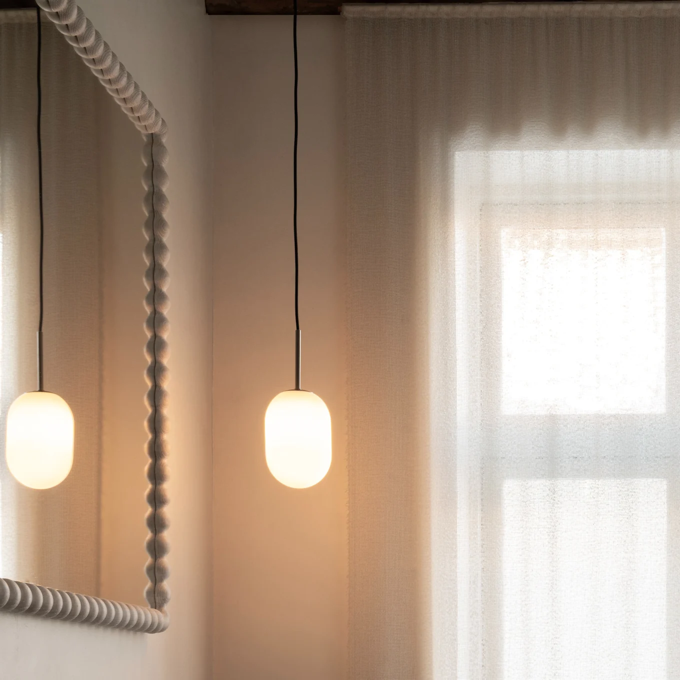 Modernt badrum: träkommod, mörk diskho, bronskran, texturerad spegel, pendellampor, skira gardiner.