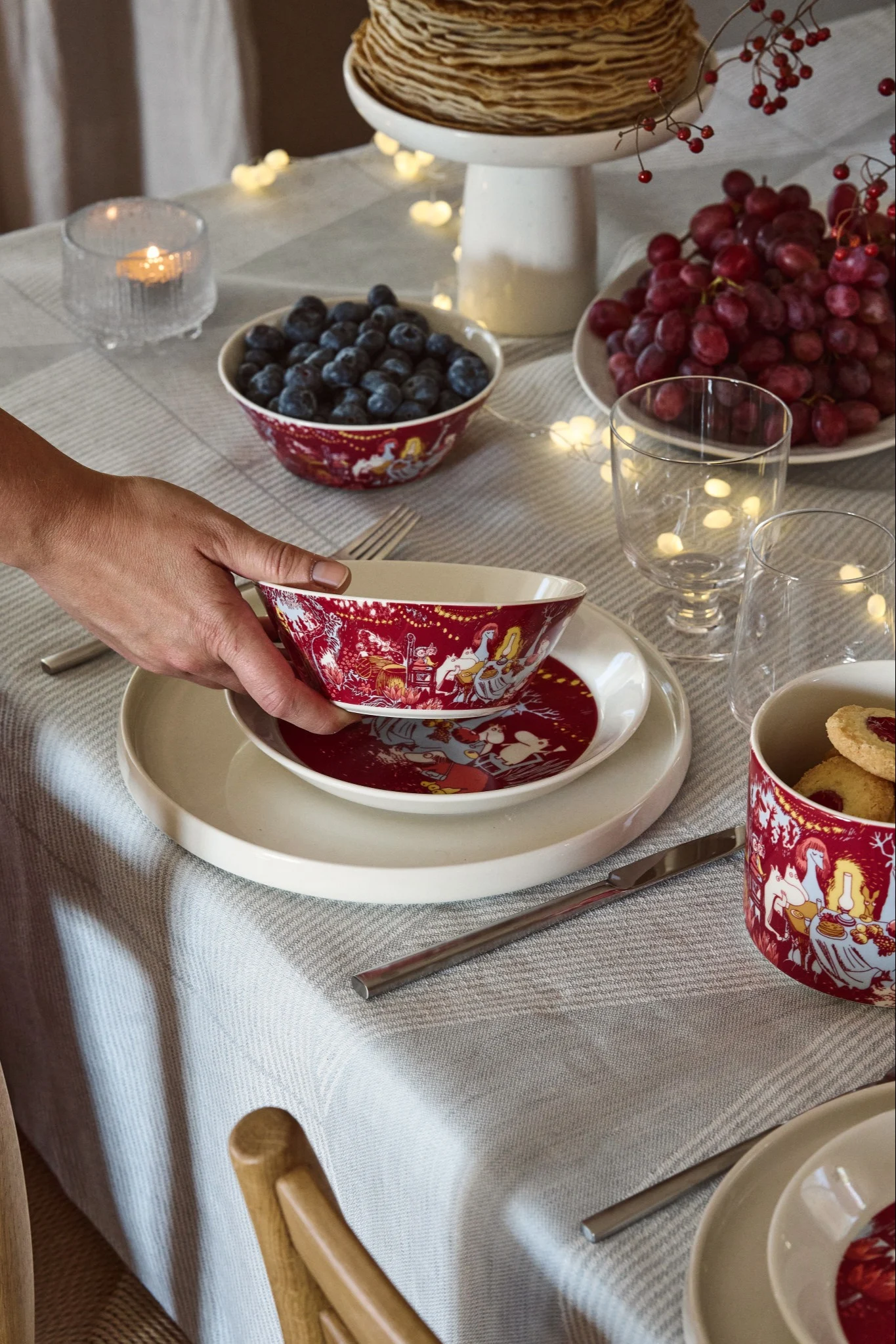 En lekfull juldukning 2025 skapas med rött porslin prytt med Muminmotiv, kombinerat med färgglada bär som sätter en varm och inbjudande ton på bordet.