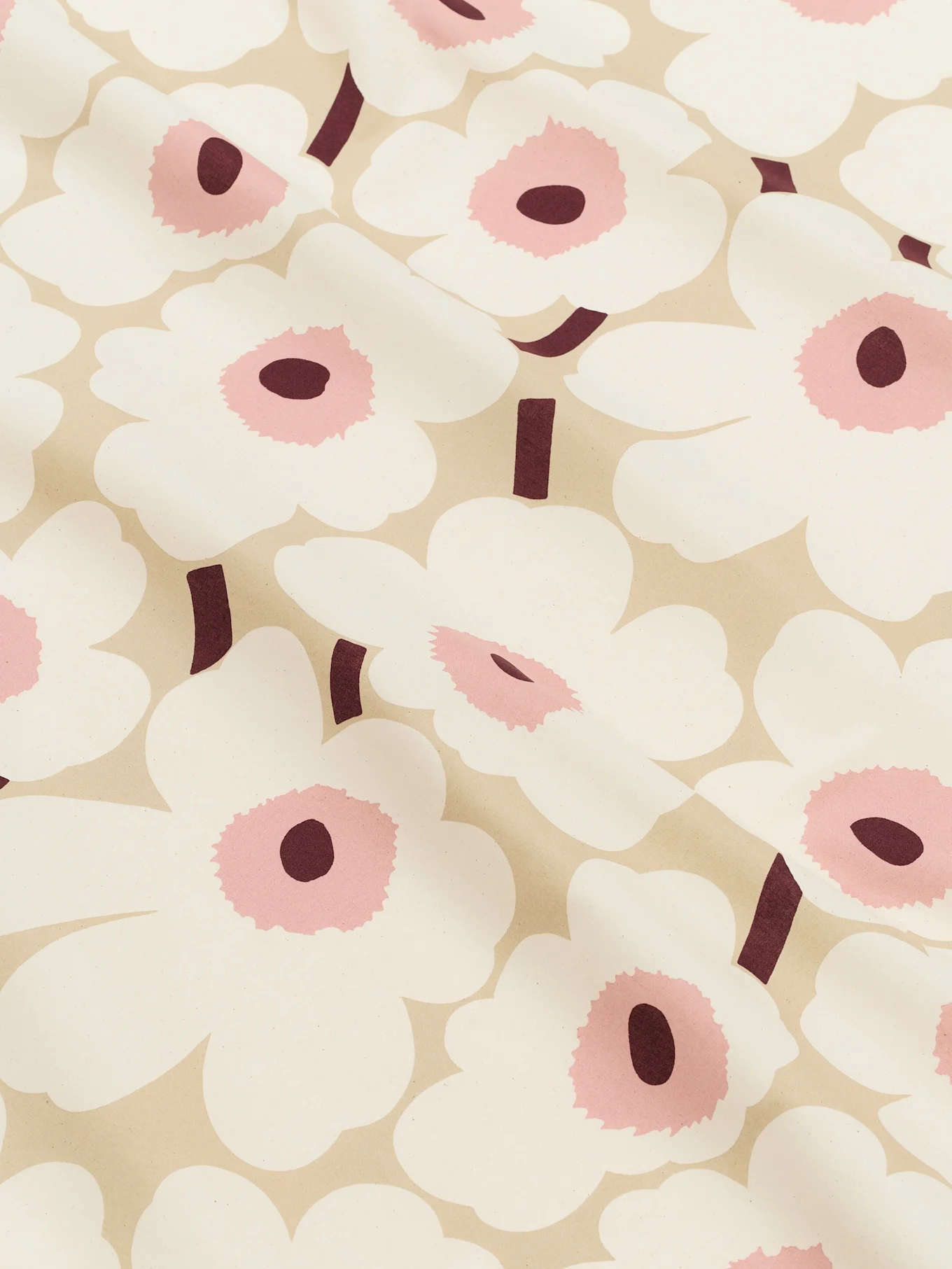 Närbild av ett ljusbeige tyg mönstrat med stora vita stiliserade blommor med rosa centrum och mörkröda stjälkar.