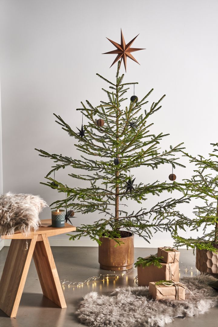 Dekorera julgranen med årets julgranspynt 2021 i 4 olika stilar enligt Nest Trends - Nurture, Share, Boost och Cultivate. Här ser du Angle pall från Muubs med Skandinavisk doftljus skog bredvid paket på en fårfäll.