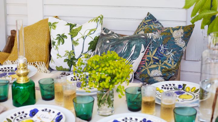 En sommarlunch inväntas och kuddar finns att luta sig tillbaka på i soffan. På bordet står gröna Kartio glas från Iittala och en oljelampa.
