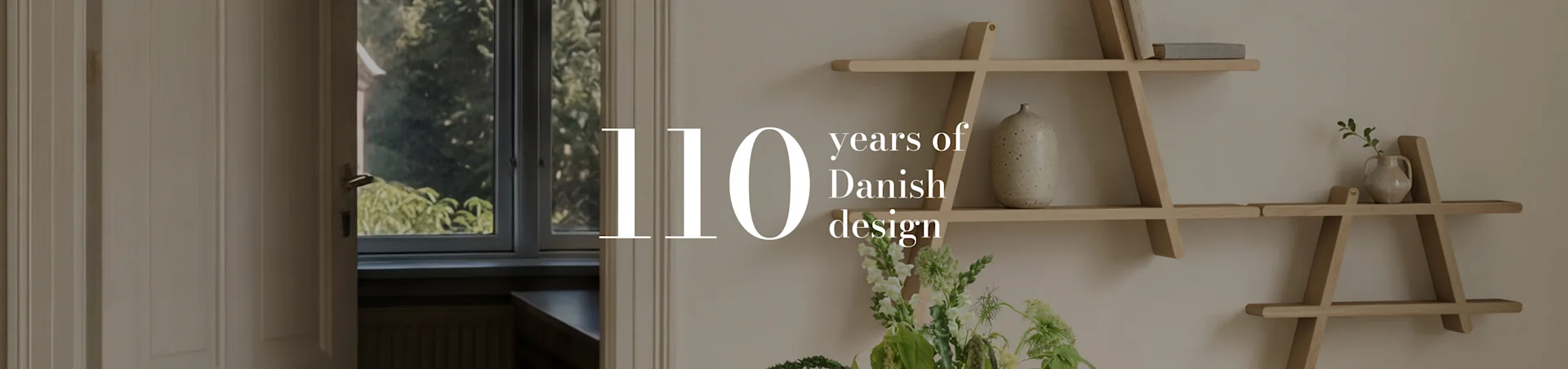 Texten '110 years of Danish design' över en interiörbild av ett rum med en geometrisk trähylla, en vas och blommor.