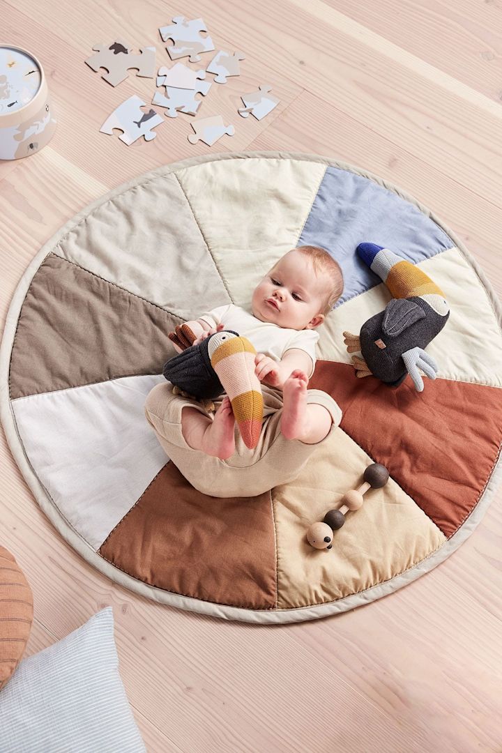 Gosedjuret Trine Toucan från OYOY ligger bredvid en bebis på babyfilten Moni. Gosedjuret är tillverkat helt av återvunnet material, vilket gör det inte bara till en användbar leksak utan också till en hållbar present till babyshower.