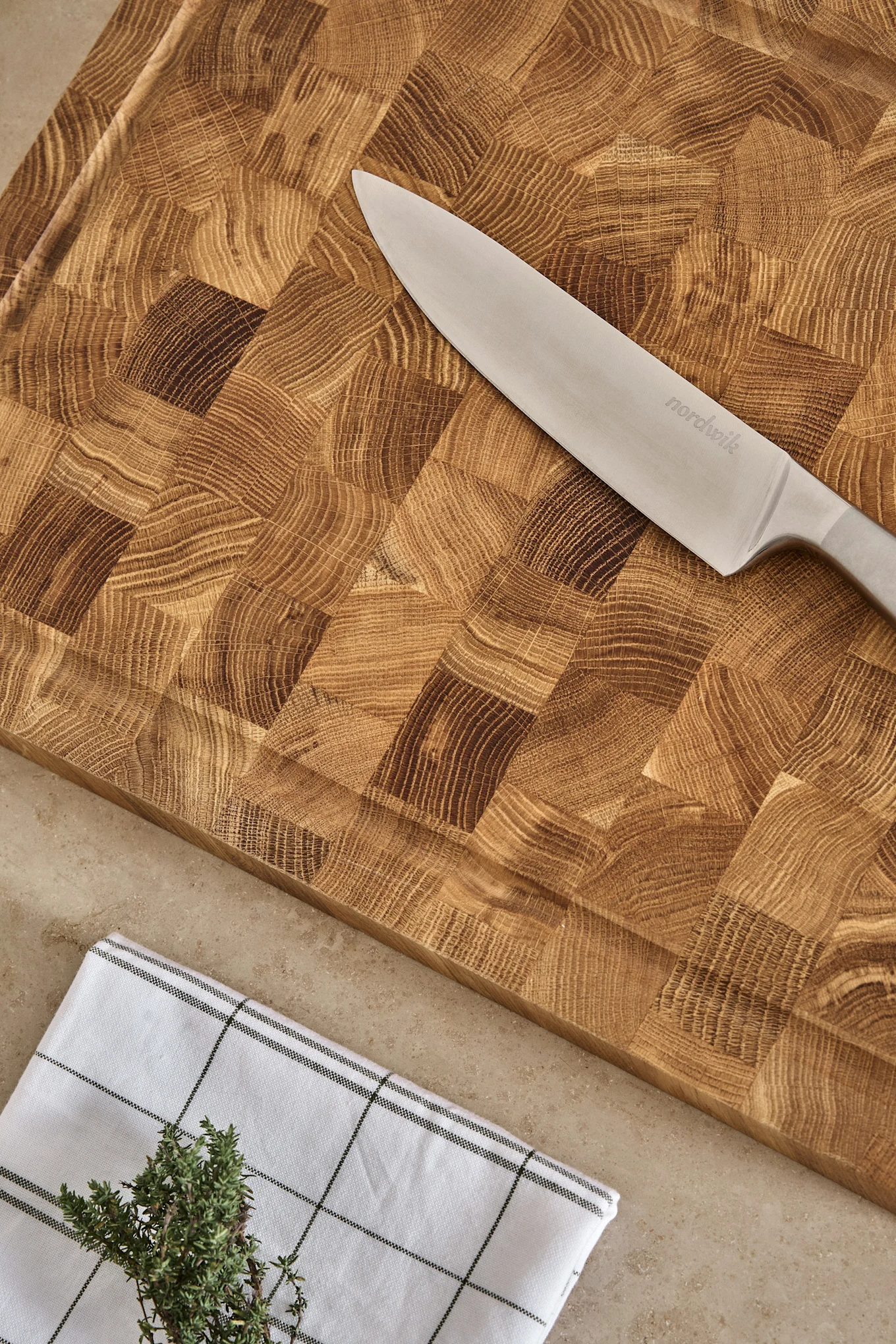 Nordwik kockkniv på en skärbräda i ändträ med rutig handduk och färsk timjan.