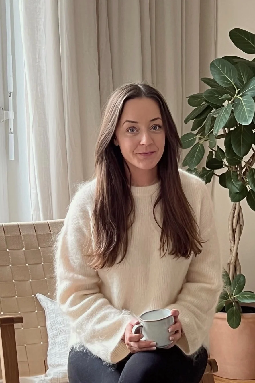 Profilbild på influencern Helena Jonsson @helenas.hem som sitter i sitt vardagsrum med minimalistisk inredning där beigt ton-i-ton och naturmaterial är temat.