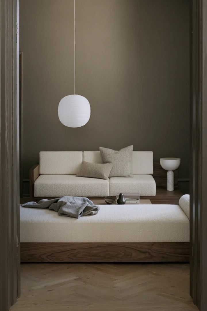 Bild som visar Lantern taklampa från New Works, en vit, oval taklampa här hängandes i vardagsrum vid ljus soffgrupp.