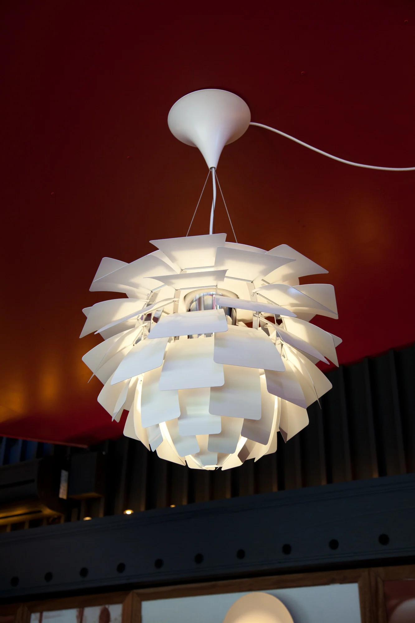 En vit PH Artichoke taklampa hänger från ett rött tak. Lampan är tillhör en klassisk designlampa.