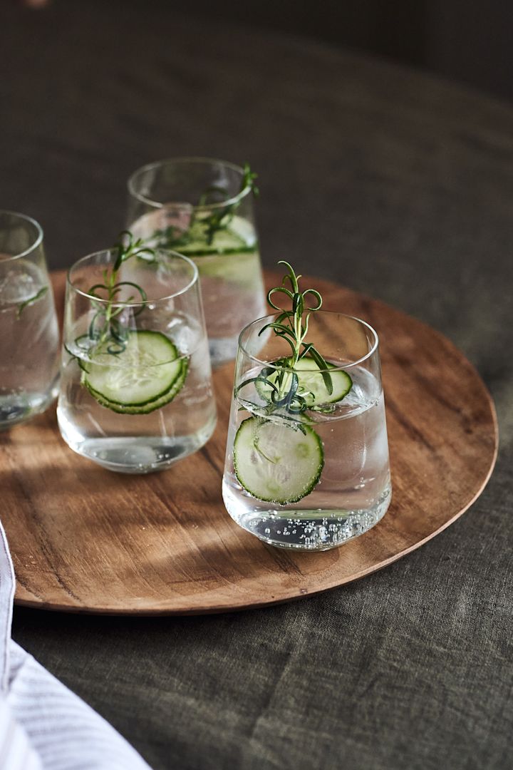 4 festliga & enkla drinkar till nyår - här ser du en fräsch gin & tonic med rosmarin och gurka i Iittala Essence drickglas på Muubs Teak tallrik.