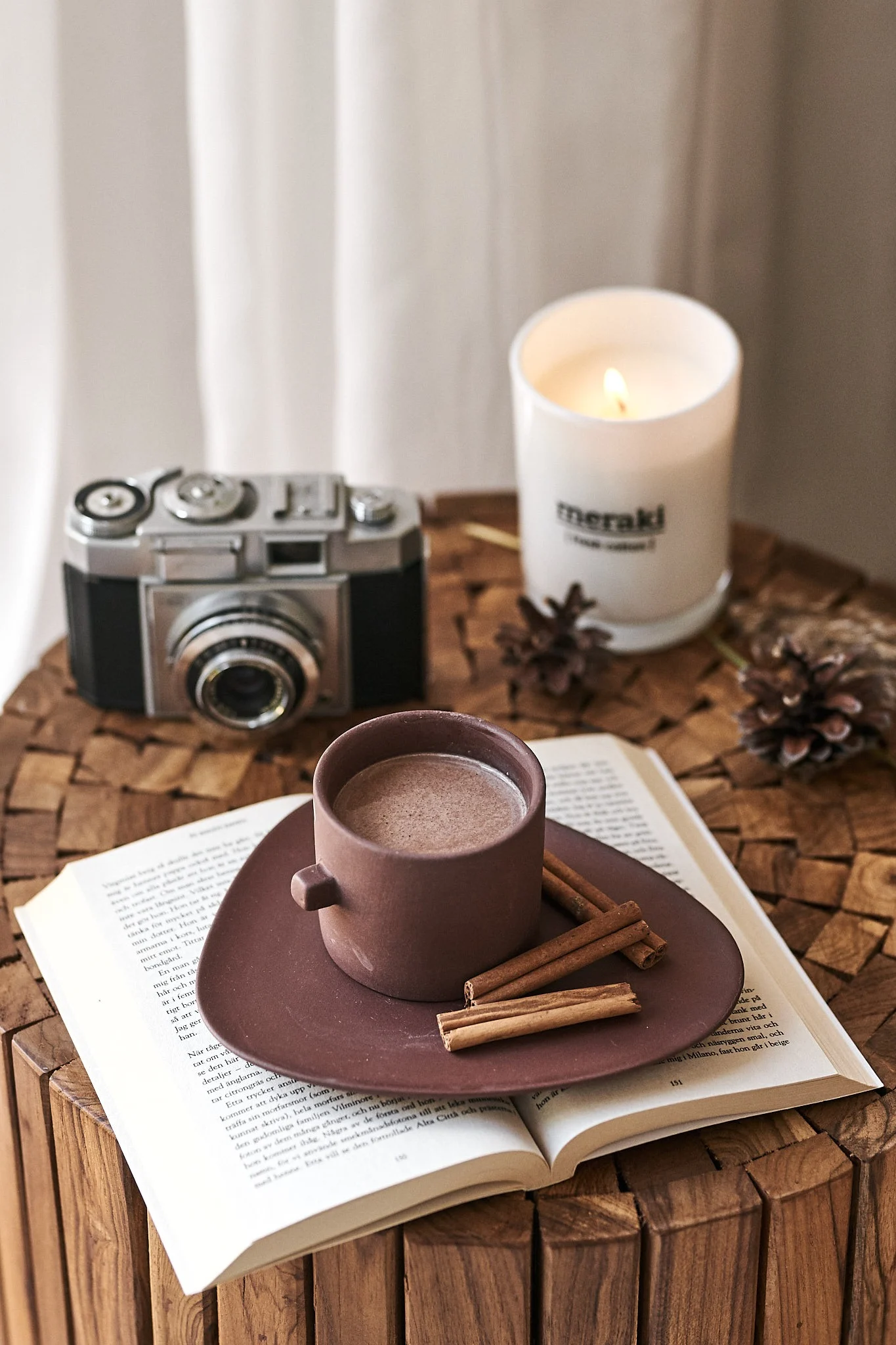 Brun kaffekopp från By On vilar på boken på sidobordet i en mysig läshörna. 