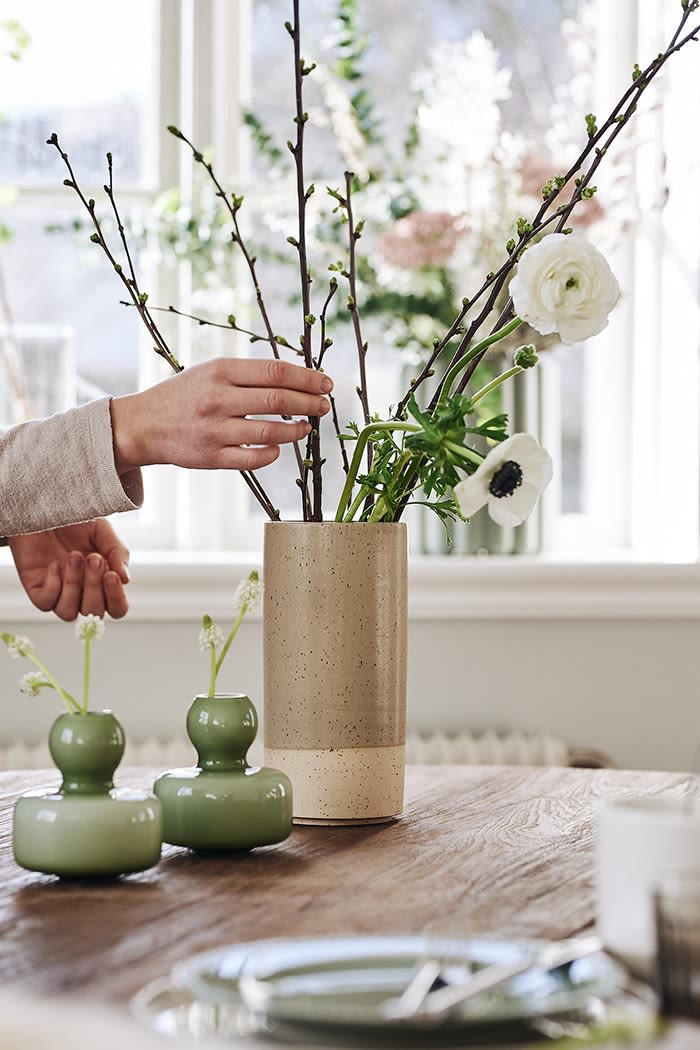 Påskinredning behöver inte vara traditionell utan kan vara avskalad som här med en rustik vas och mindre vaser i grönt fyllda med vårblommor. 