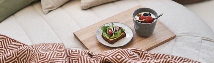 Frukost på sängen serverad på träbricka med mjuk pläd bredvid. 