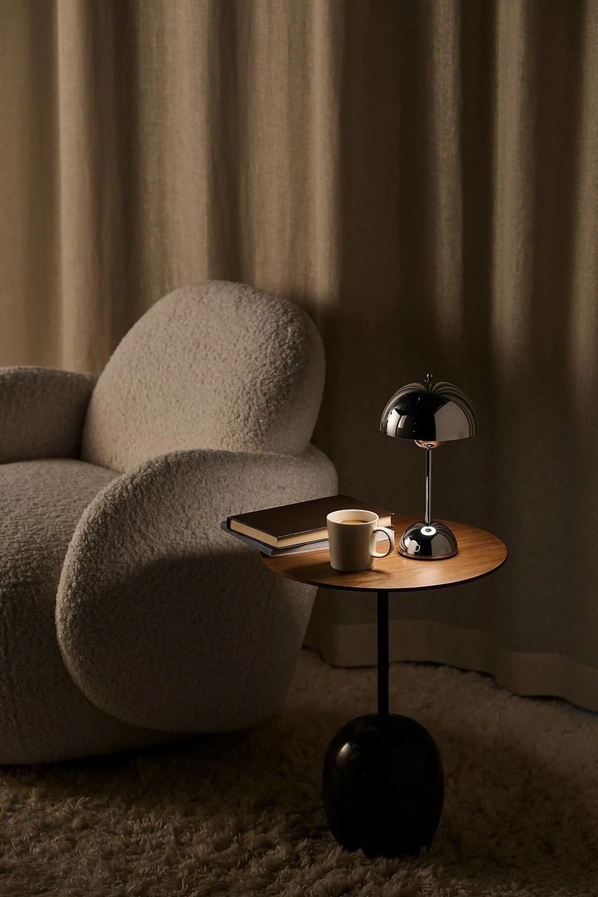 Bredvid Mo-fåtöljen från 1898 står ett soffbord med en bok, en kopp kaffe och den kromfärgade Flowerpot-bordslampan från &Tradition.