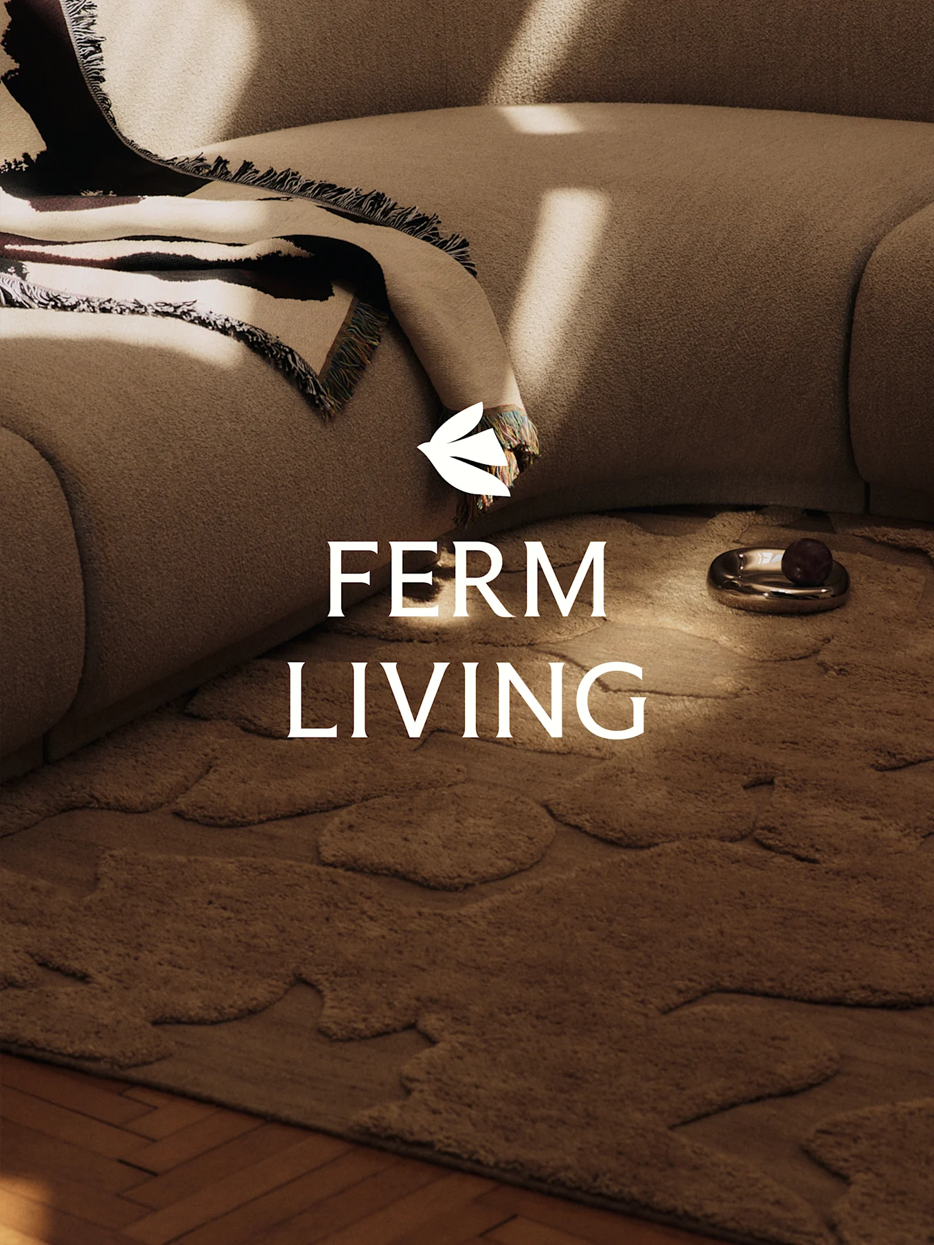 En mysig scen med en ljusbrun texturerad soffa, en mönstrad filt, en brun matta med organiska former och en dekorativ skål.