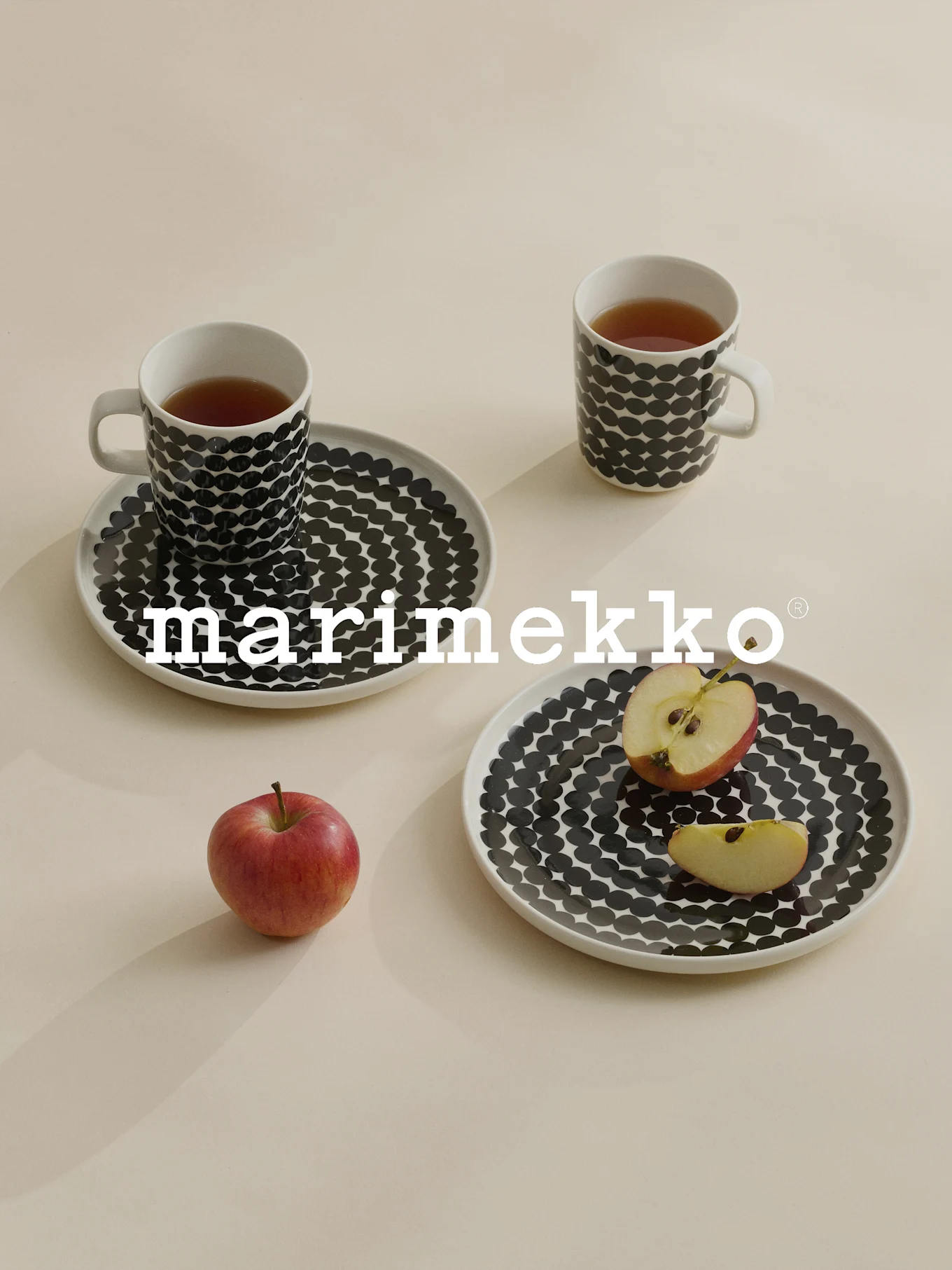 Två muggar och tallrikar med svarta prickar, te, rött äpple, Marimekko-logotyp.