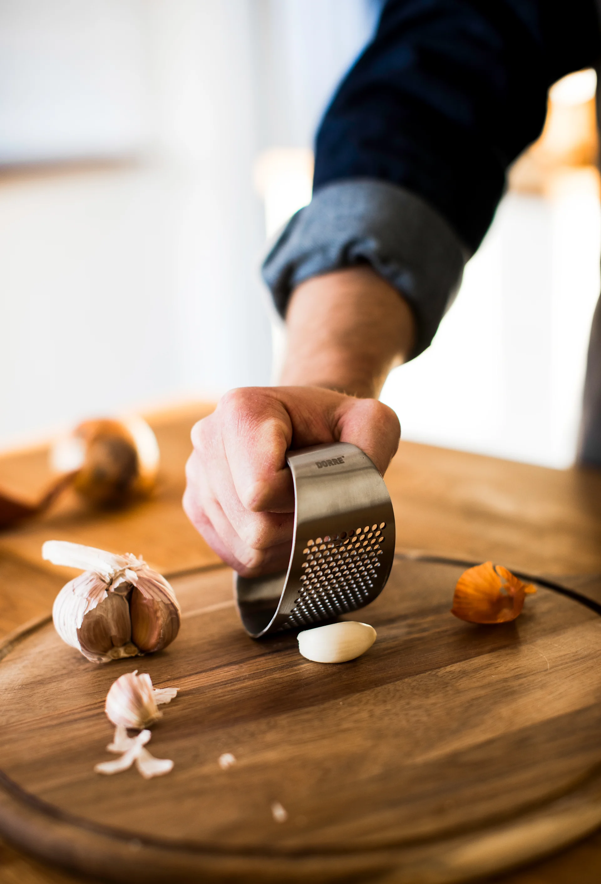 En hand pressar en vitlöksklyfta med en vitlökspress i rostfritt stål på en skärbräda i trä.