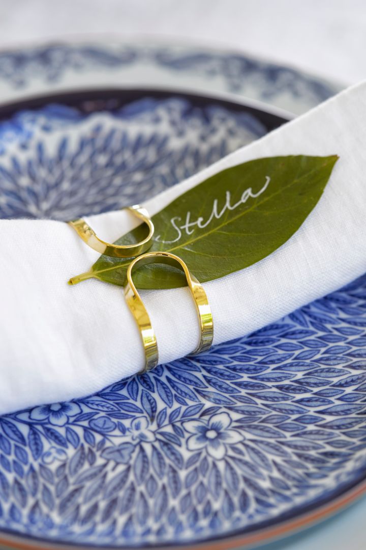 Midsommardukning med blåvitt porslin och vit linneservett ihoprullad i en servettring i mässing.