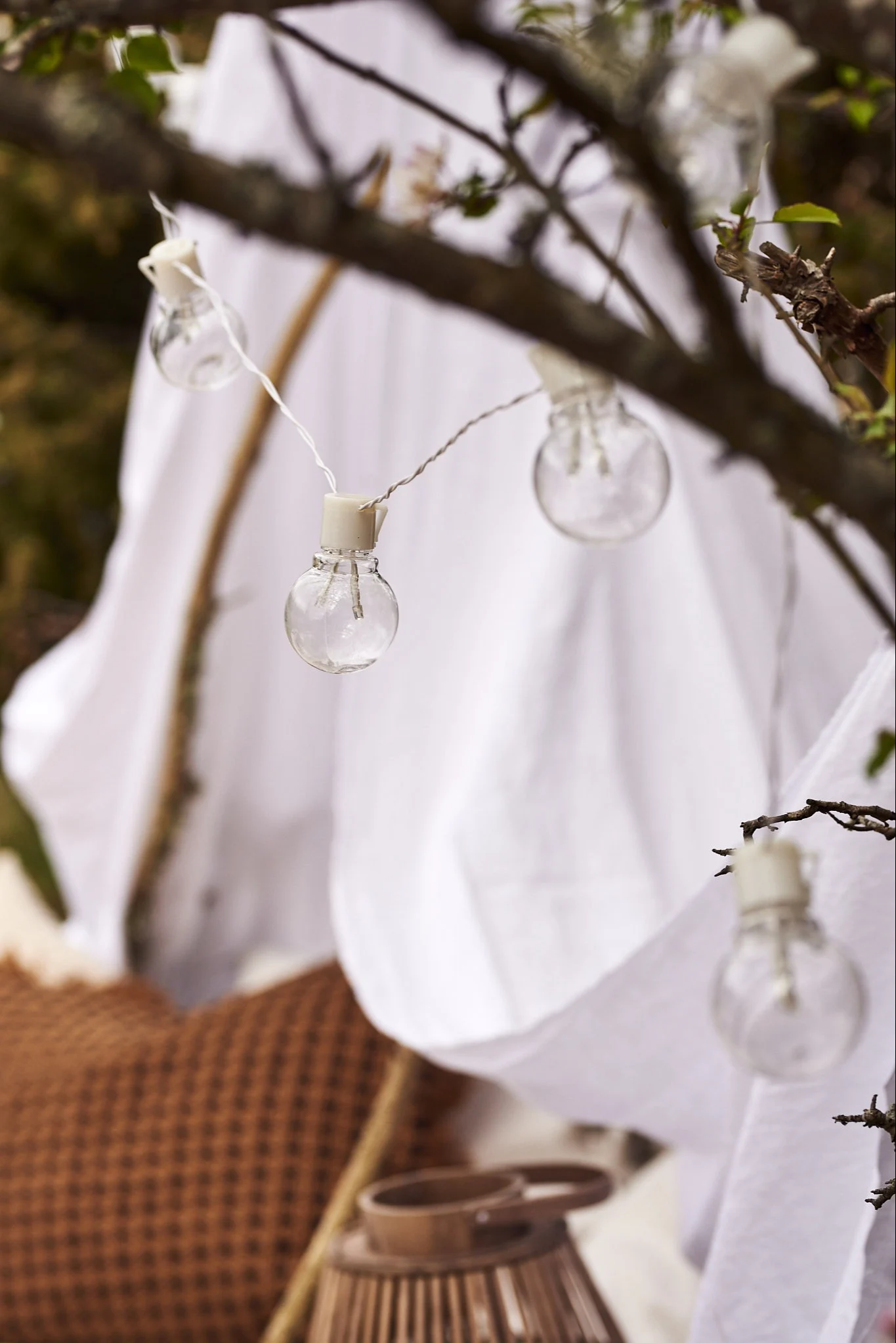 En vit ljusslinga hänger över litet tält i skogen.