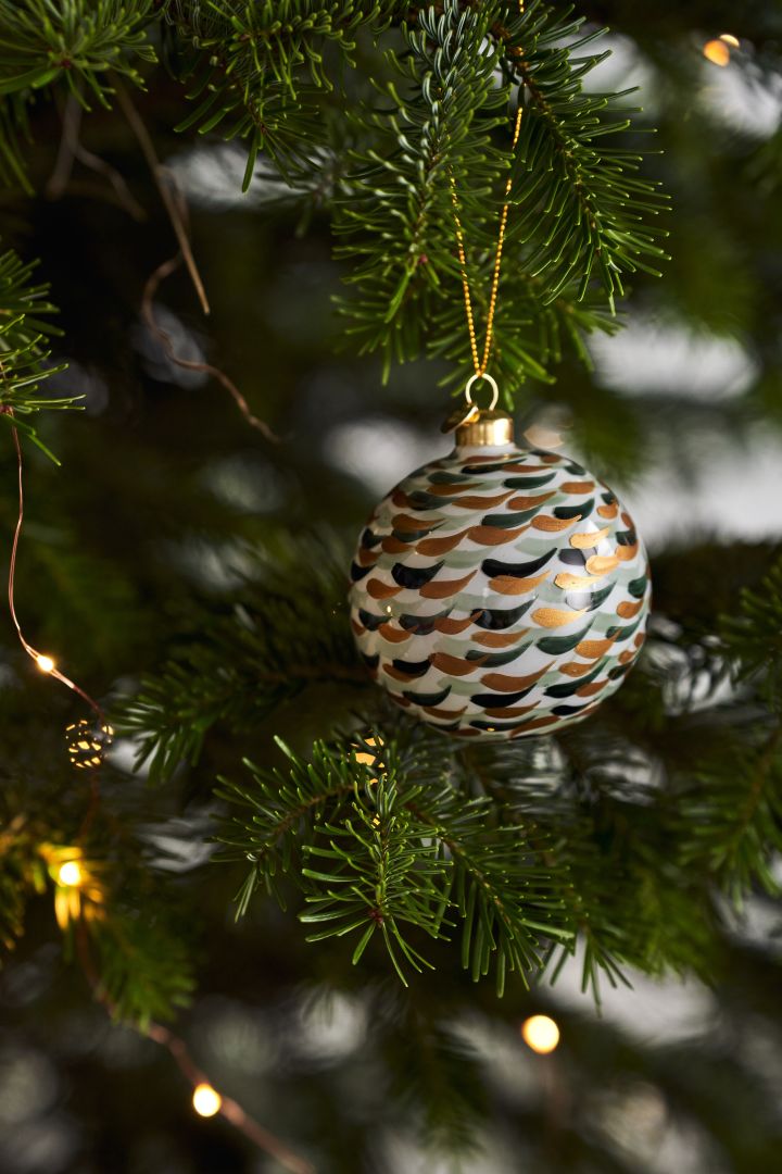 Dekorera julgranen med årets julgranspynt 2021 i 4 olika stilar enligt Nest Trends - Nurture, Share, Boost och Cultivate. Här ser du Souvenir julkula med penseldrag från Holmegaard.