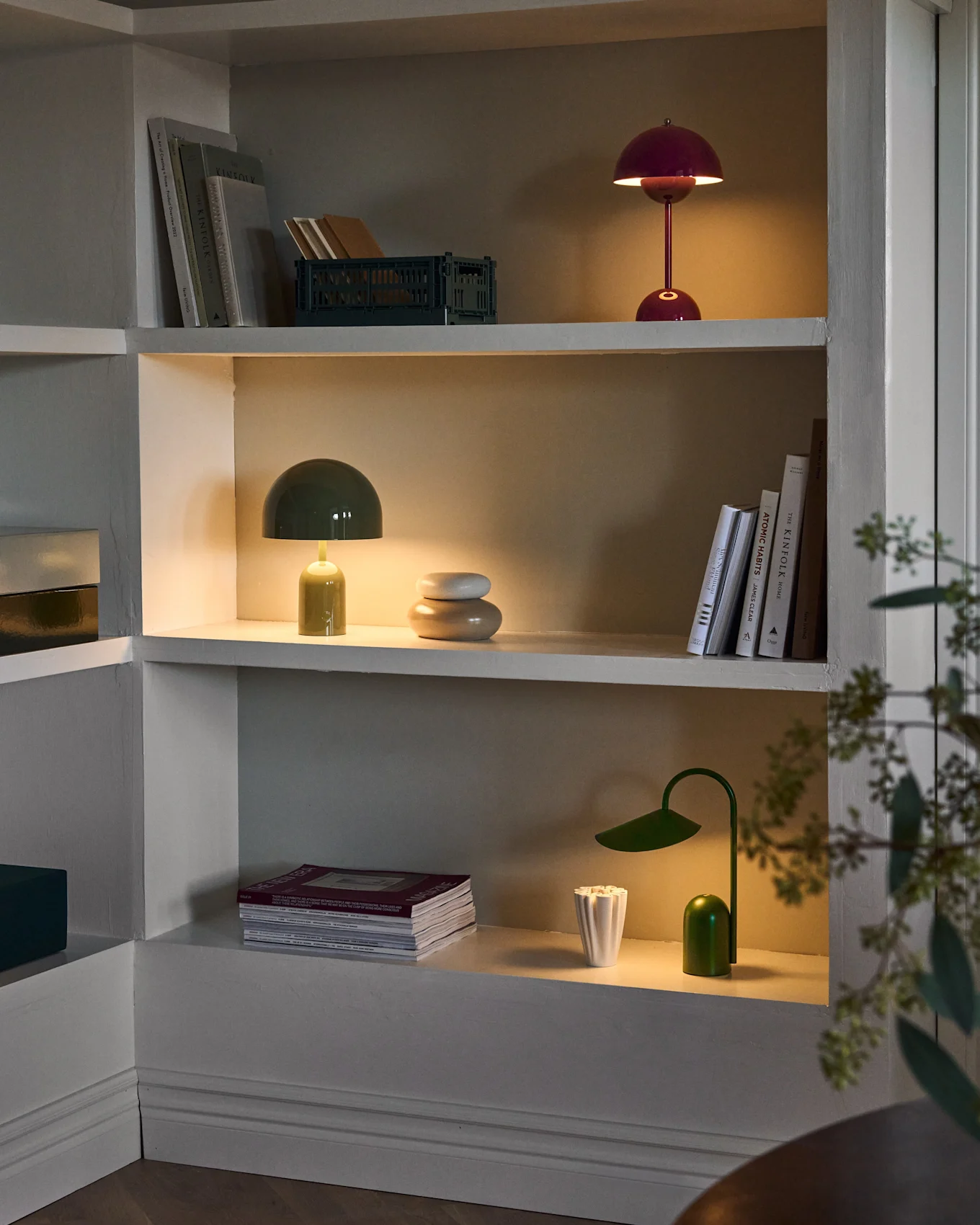 Upplysta hyllor i inbyggd enhet, med röda och gröna svamplampor, grön skrivbordslampa, böcker och inredning.
