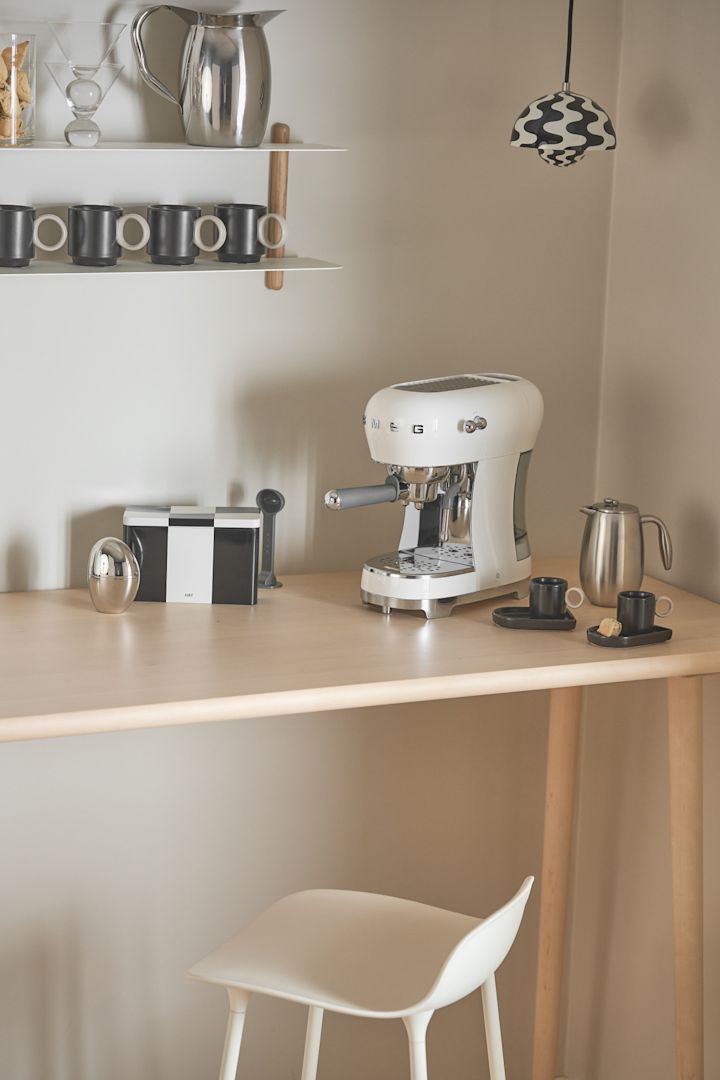 Kaffemaskinen från Smeg, som här står i ett hörn, är särskilt lämplig för en kaffebar i hemmet, med en Flowerpot-pendellampa från &tradition som belysning.
