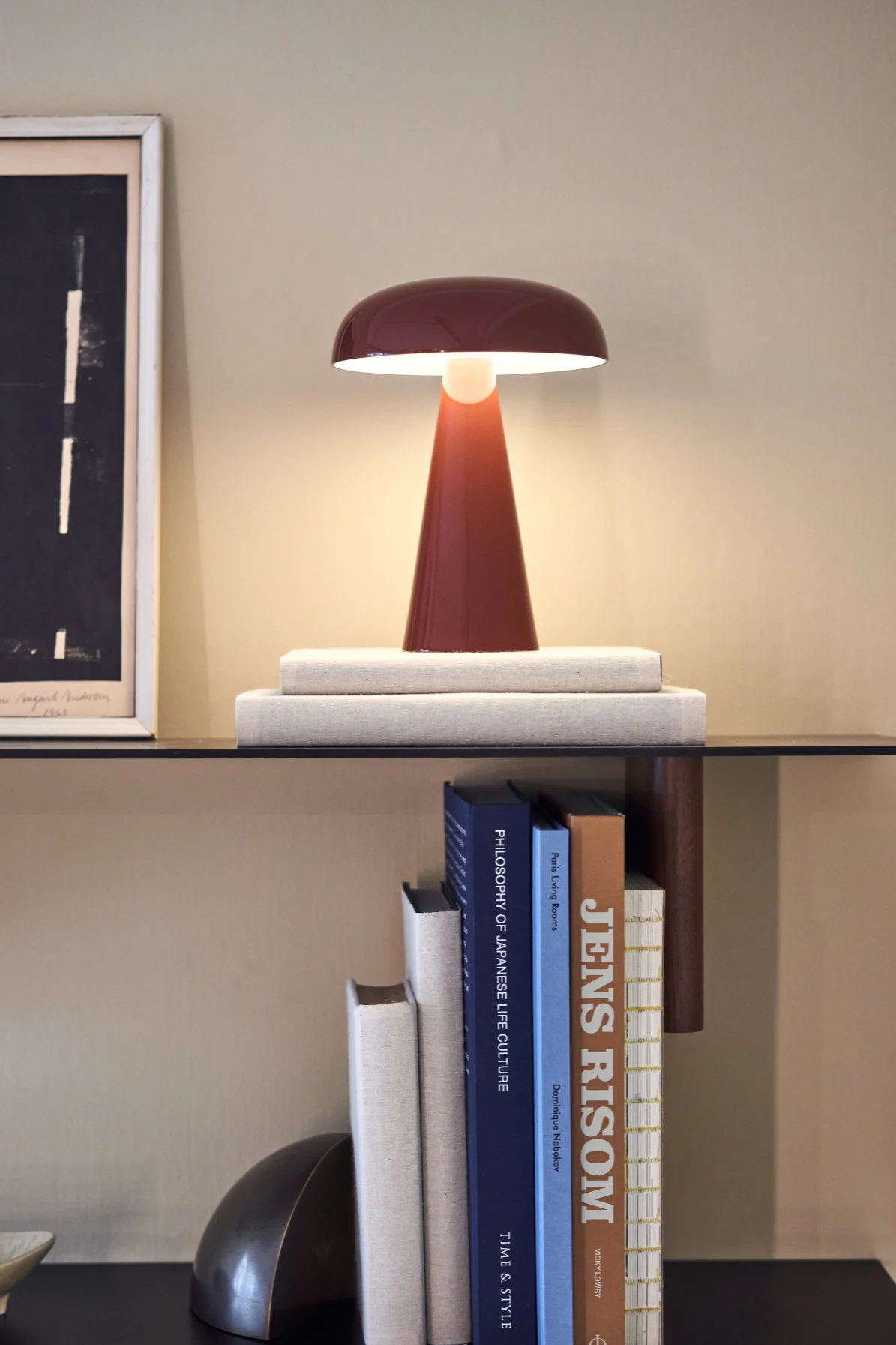 Como portabel och uppladdningsbar lampa i rött från &tradition på en stilren bokhylla omgiven av böcker. 