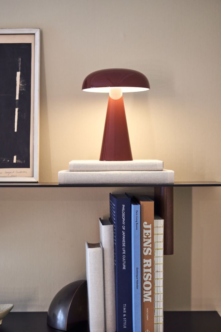 Como portabel och uppladdningsbar lampa i rött från &tradition på en stilren bokhylla omgiven av böcker. 