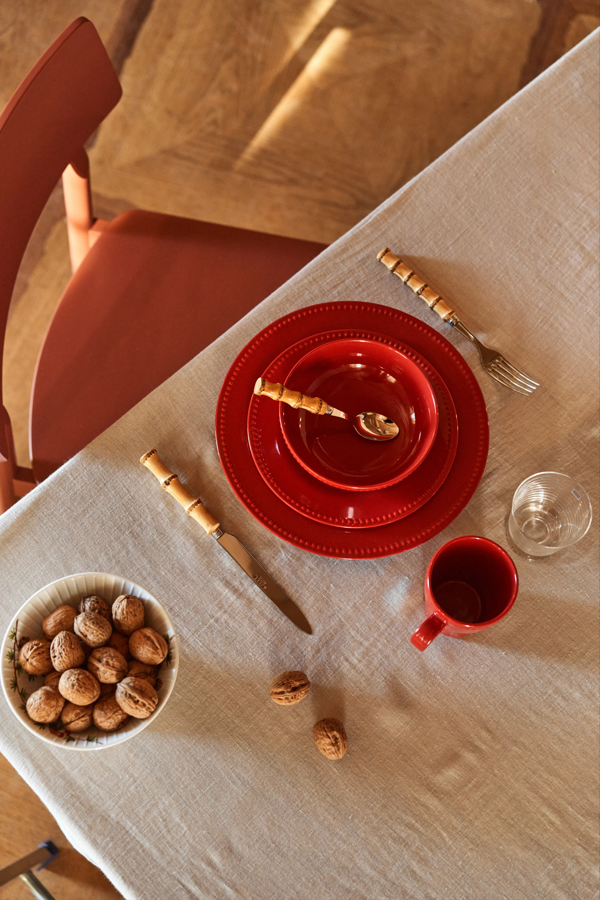 Ett avskalat rött porslin med tallrikar i olika storlekar, kombinerat med en skål fylld med valnötter – en stilren tolkning av juldukningen 2025