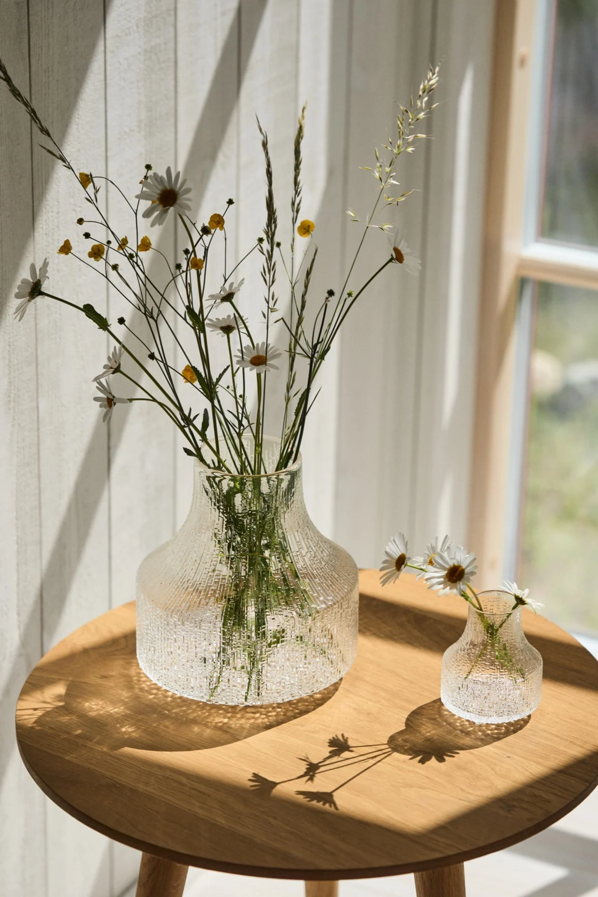 Den bästa vasen för små buketter och enskilda blommor är en liten eller en minivas som Ultima Thule-vaserna som du ser här i solskenet på ett bord. 