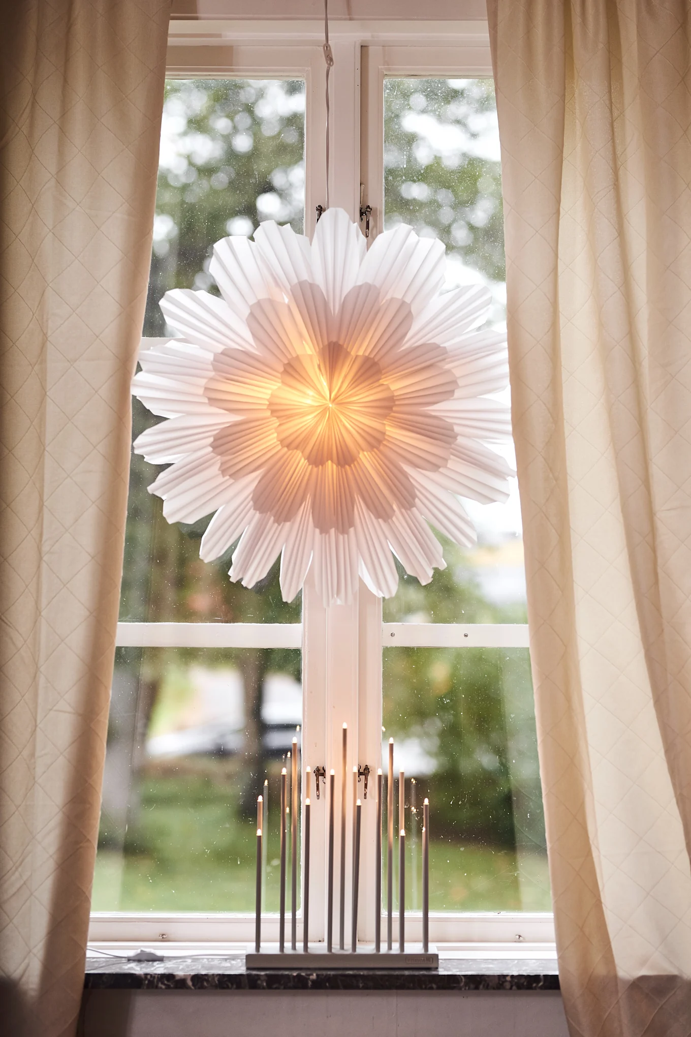 För att fira första advent kan du adventspynta hemmet. På bilden syns adventsstjärnan Snöblomma från Watt & Veke hängande i fönstret tillsammans med ljusstaken Elflugan som står på fönsterbrädan. 