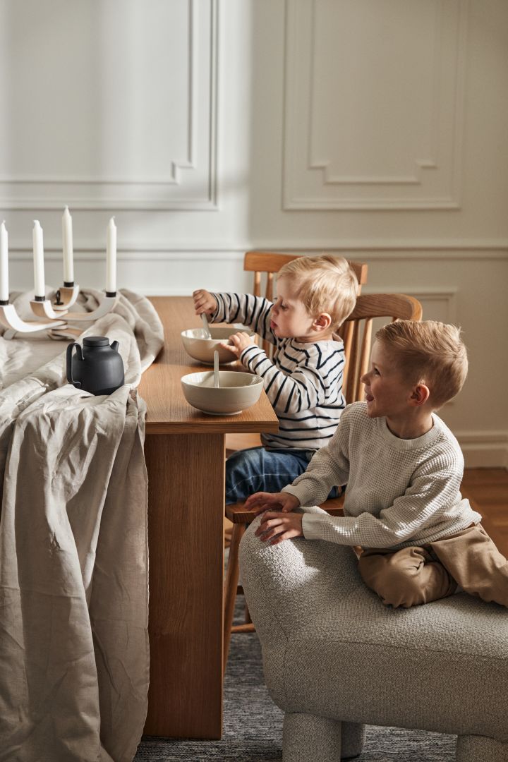 Två pojkar sitter vid middagsbord från Design House Stockholm, i bild syns även Lulu-sittpuff samt skålar från serien NM&Sand. 