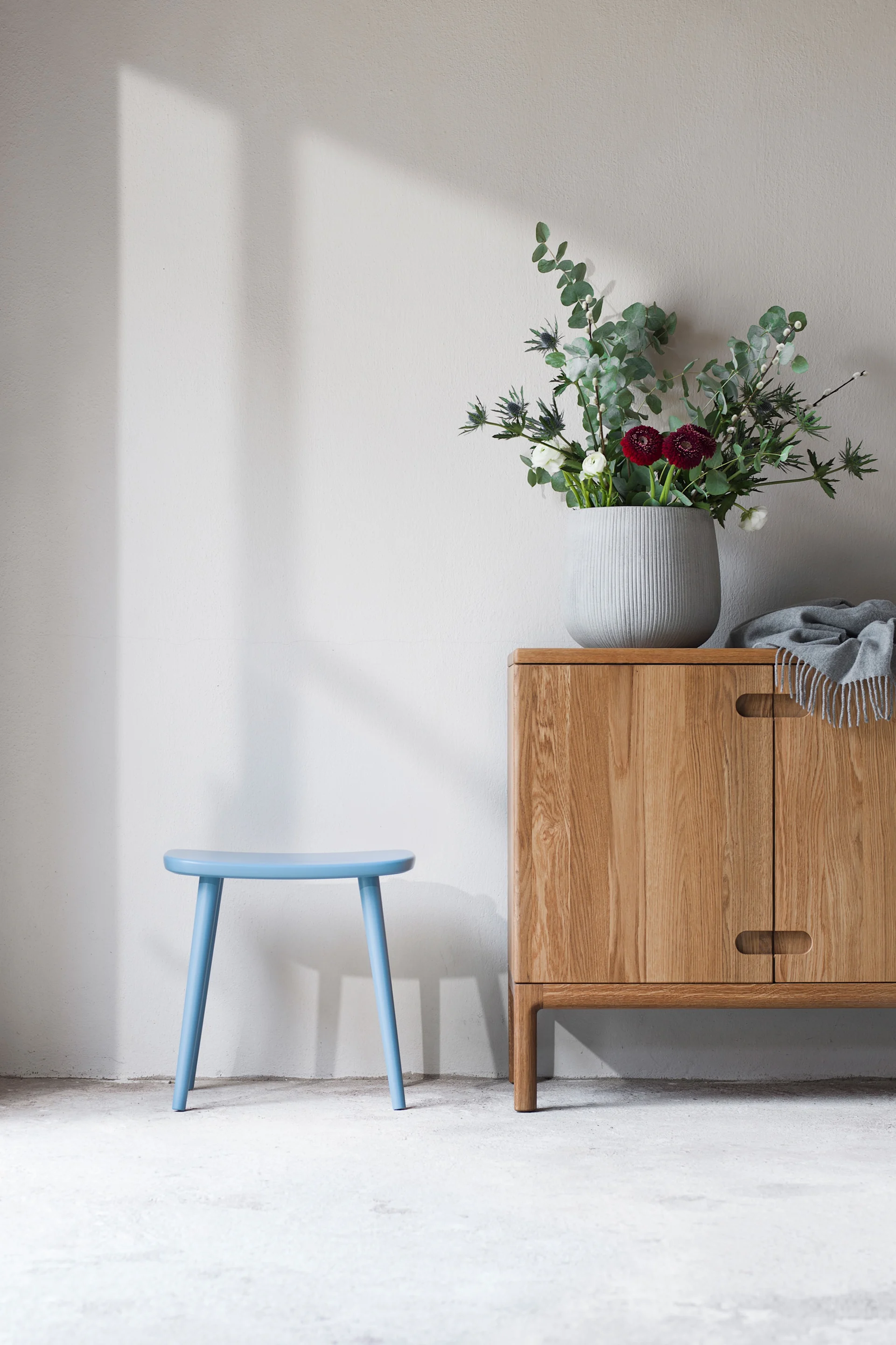 Palle pall från Stolab i en ljusblå färg står bredvid en skänk i trä i ett naturfärgat rum.