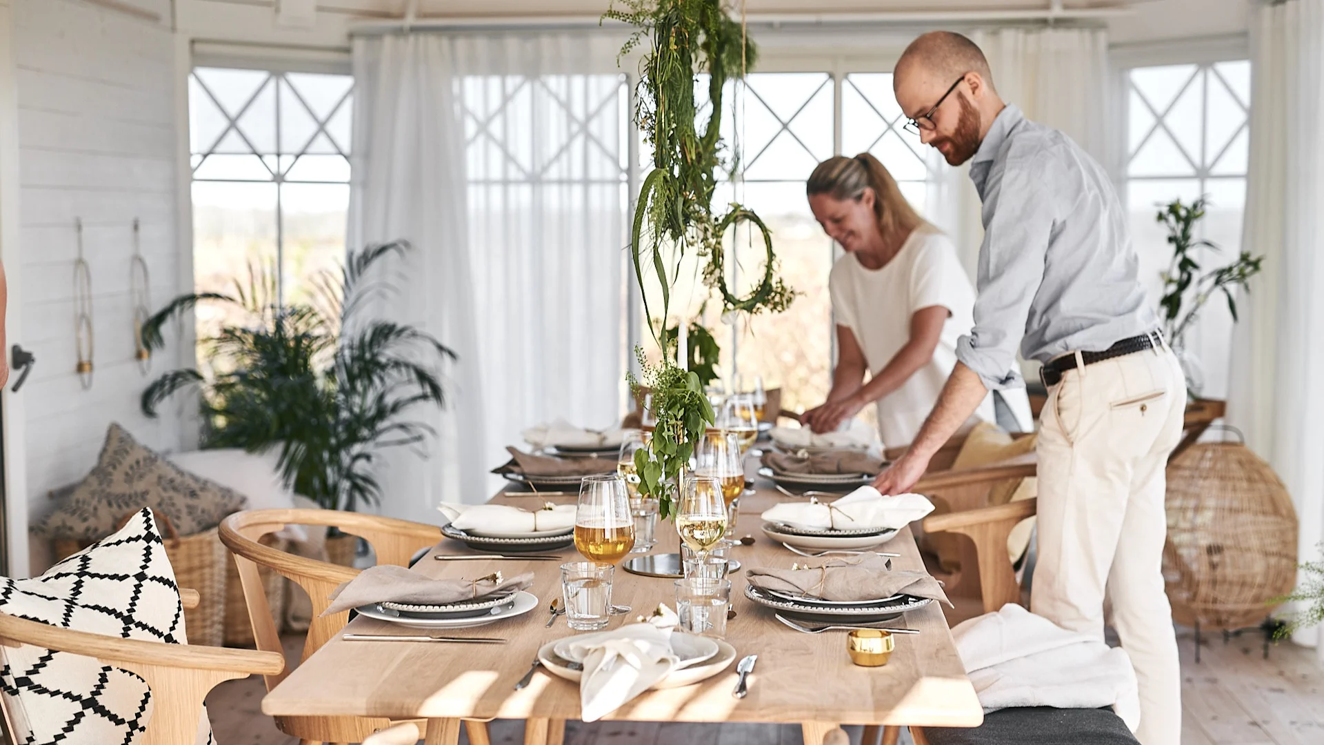 Värdparet är i full gång med att duka upp sin sommardukning där neutrala färger i vitt och beigt dominerar och porslin blandas så alla får plats.