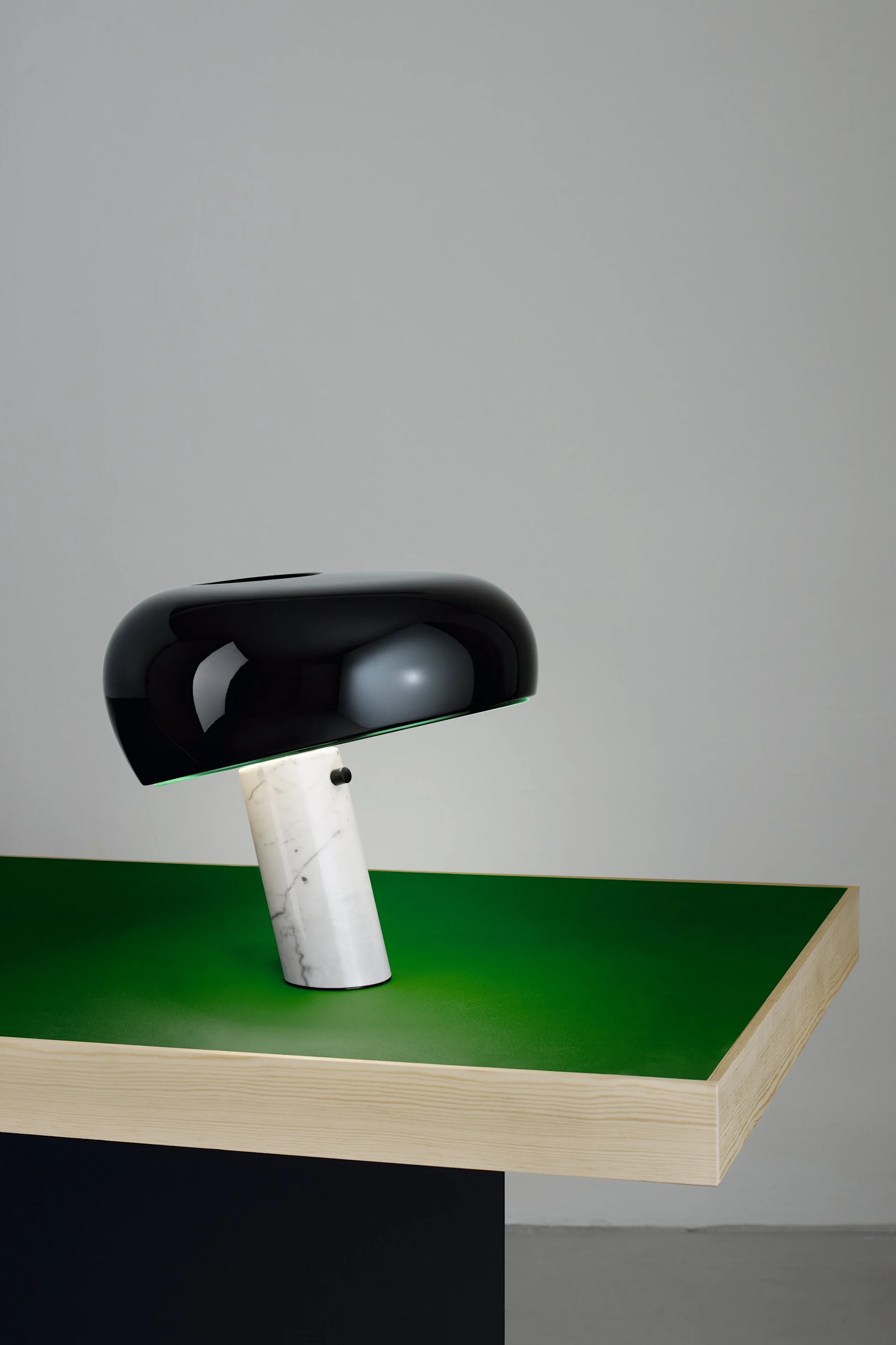 En Snoopy bordslampa från Flos i svart och marmorfot står på ett avskalat grönt bord och visar på en klassisk designlampa.