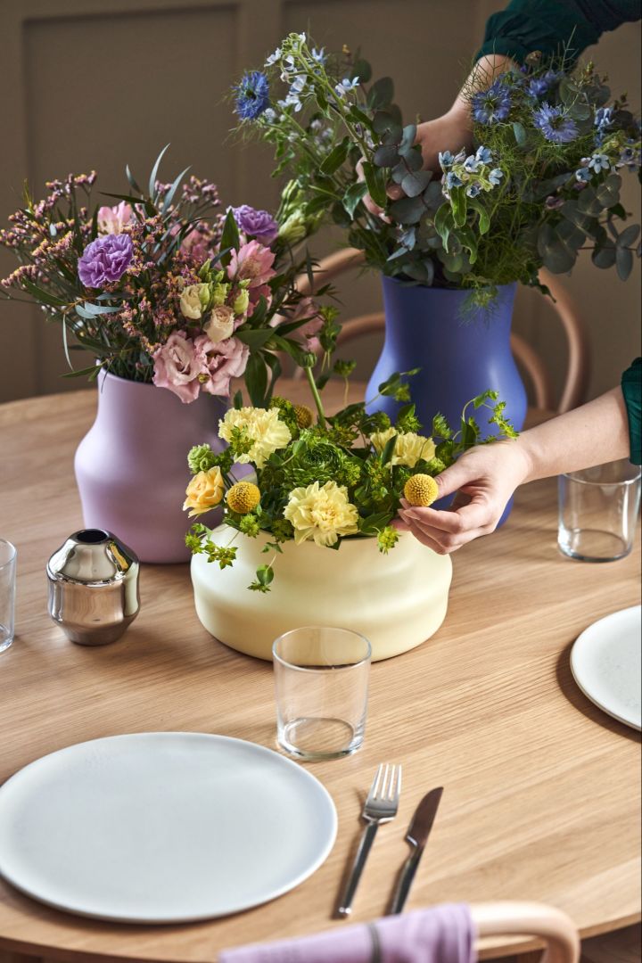 Dorotea-vaserna på ett bord med enkel dukning. Här ser du de tre Dorotea-vaserna i gult, syrénlila och kleinblå. I vaserna blombuketter som matchar färgerna på vaserna.