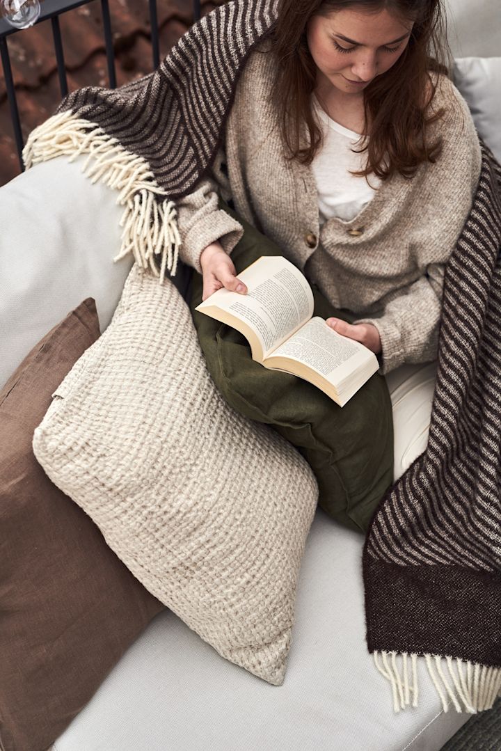 En kvinna sitter i en soffa på balkongen och läser en bok.