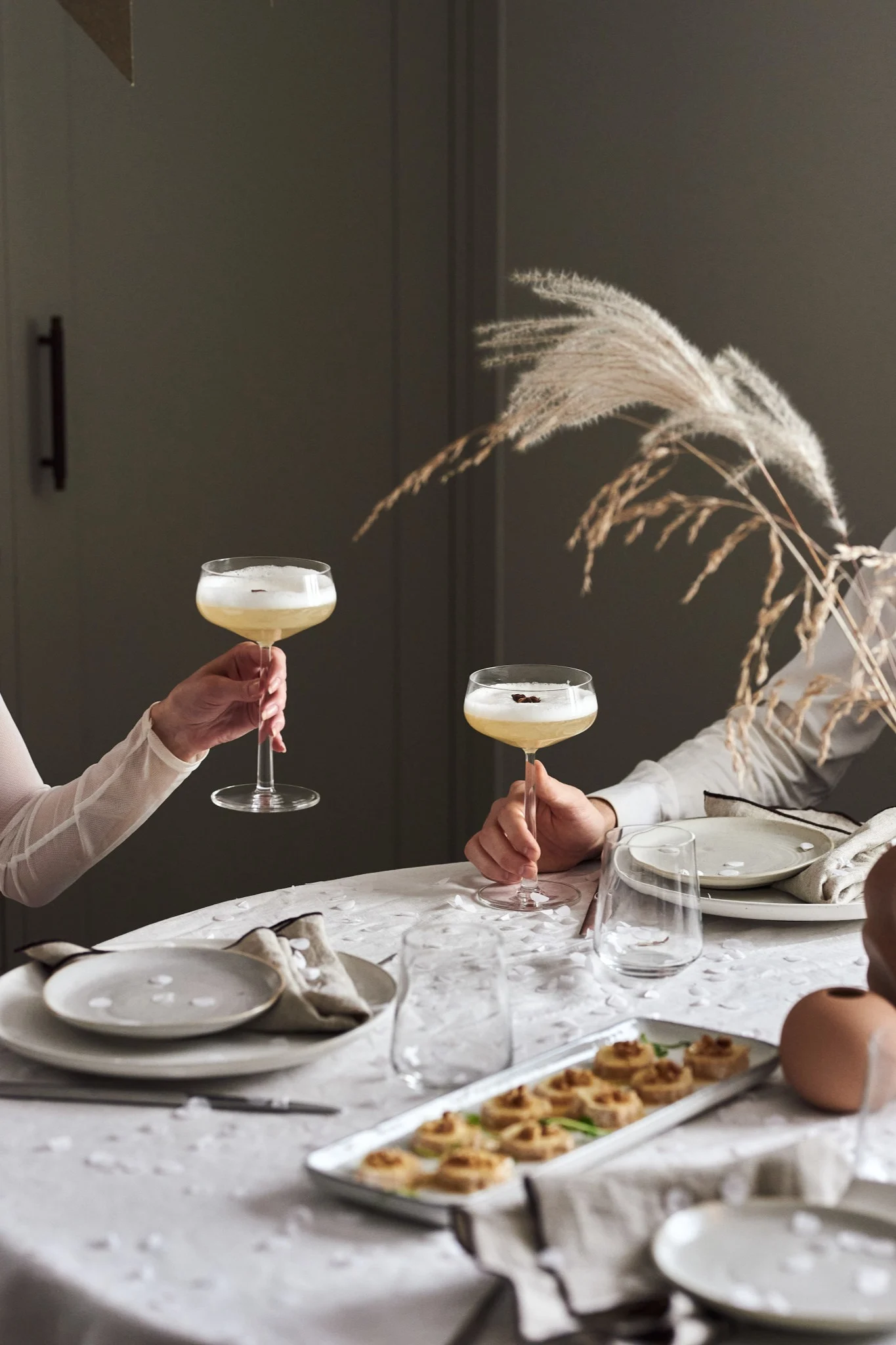 Två personer skålar runt ett bord där det serveras ett tilltugg eller efterrätt med chevrétårta.