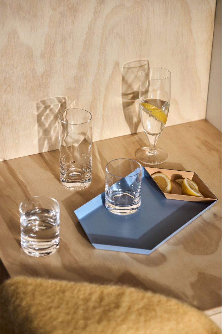 En kollektion av vattenglas och ölglas från serien Chateu från Kosta Boda på en blå, fyrkantig bricka från HAY. 