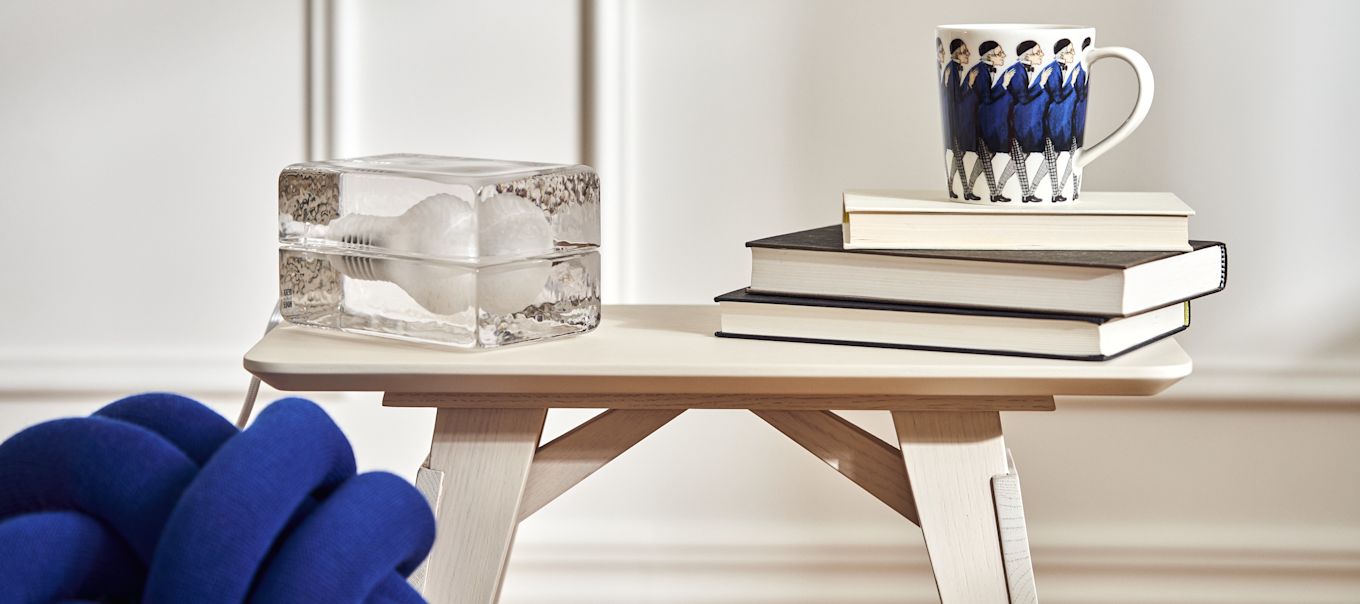 Bord i vit ek från Design House Stockholm, på det vilar lampan Block och Elsa Beskow-muggen Farbror Blå på trave böcker i stilren vardagsrum.