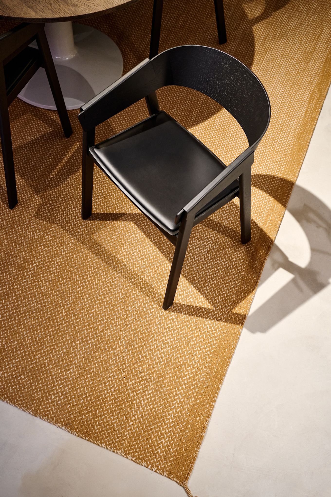 Den svarta Cover-fåtöljen med lädersits från Muuto står på en senapsfärgad matta.