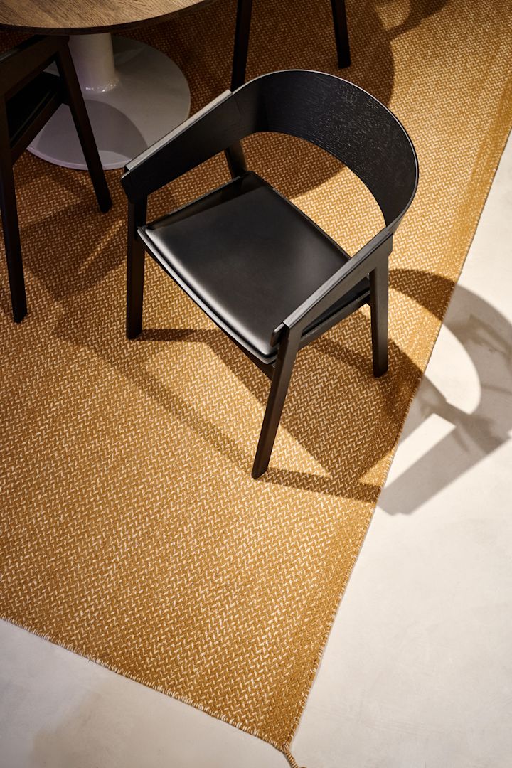 Den svarta Cover-fåtöljen med lädersits från Muuto står på en senapsfärgad matta.